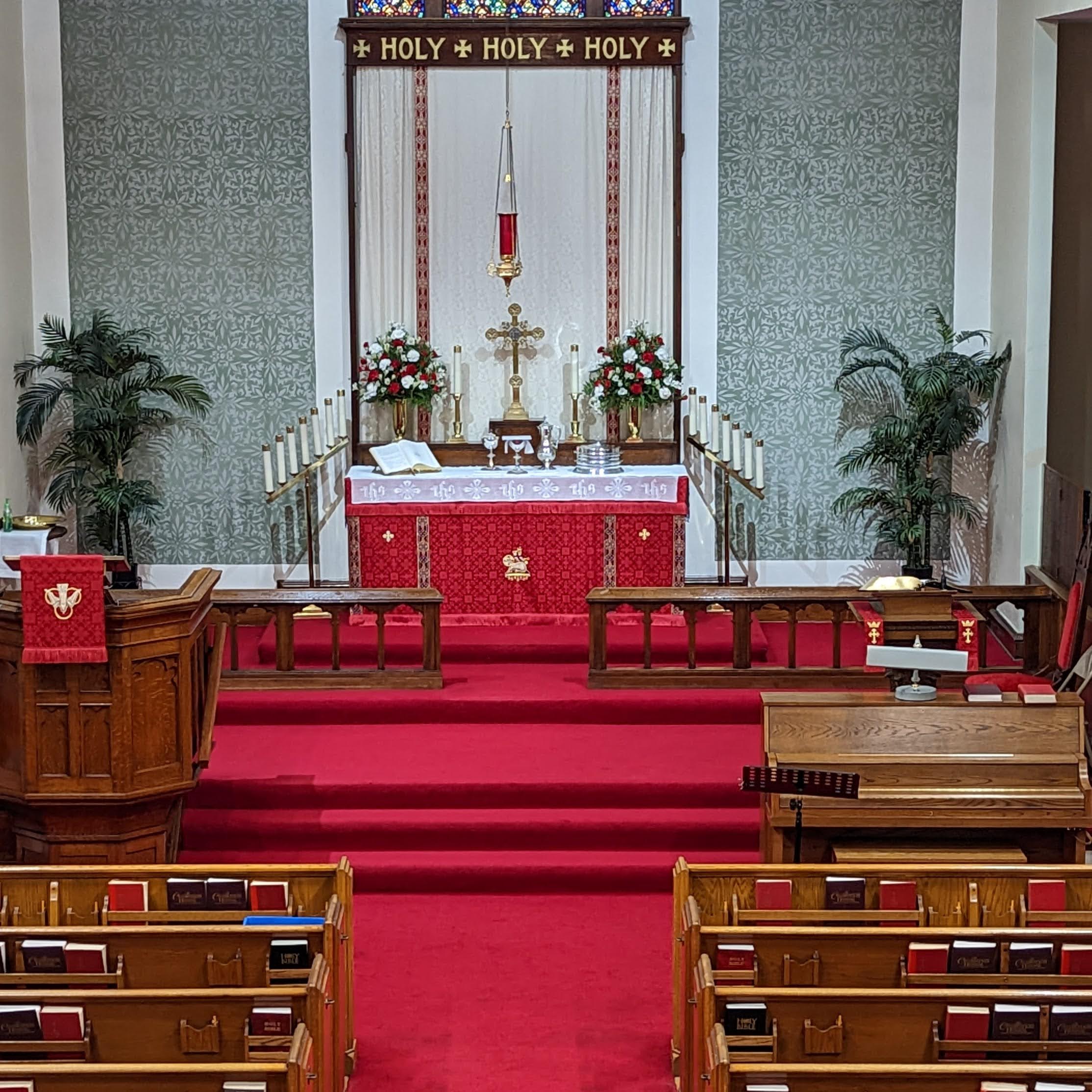 A Priest in a red chasuble standing in an empty gothic church.